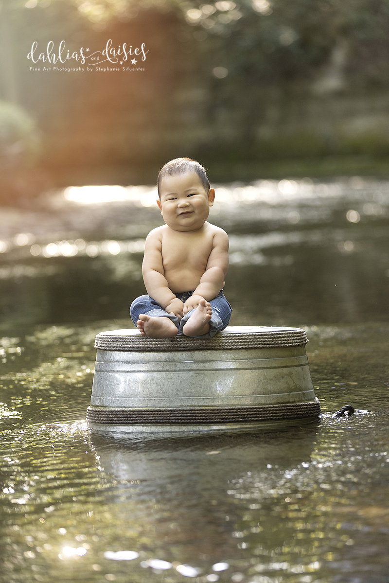 9 month old baby boy sits on tub in creek