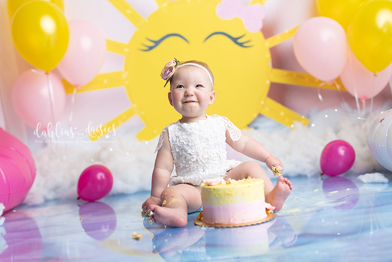 Baby girl smiles at her 1st birthday cake smash photo session