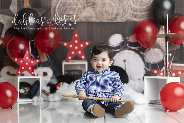 Baby holding drum sticks at first birthday cake smash photography session.
