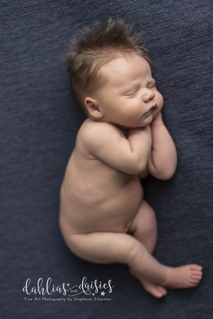 Newborn boy with gorgeous hair laying on blue fabric