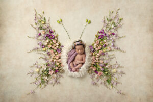 Newborn girl laying on white fur posed with purple florals to look like a butterfly