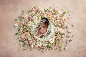 Newborn girl wrapped in light green laying in basket surrounded by pink and peach florals