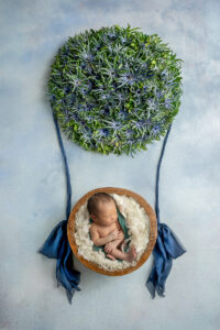 Newborn boy in bowl with blue and green flowers serving as hot air balloon