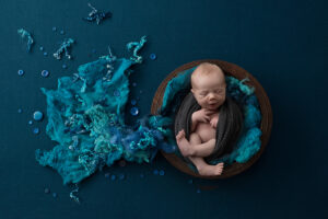 Newborn boy in bowl surrounded by blue felts