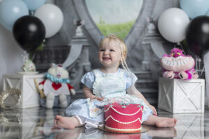 Girl smiles at mom at her Alice in Wonderland themed cake smash