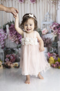Baby girl standing in pink dress holding on to moms hand