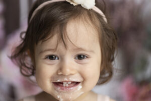 Close up of baby girls face with cake on it