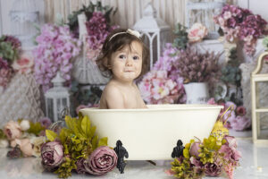 Baby girl makes a funny face splashing in the tub at her first birthday cake smash