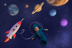 Newborn boy wearing cozy blue footed onesie floats in space