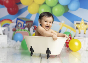 12 month old boy laughs while splashing in the tub at his cake smash