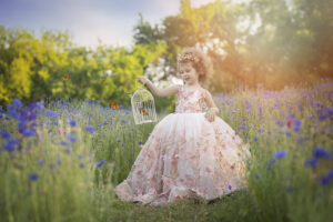 Young girl holds a birdcage full of butterflies in a wildflower field