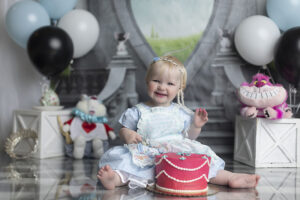 Sweet 12 month old baby smiles before eating cake at her Alice in Wonderland Cake Smash
