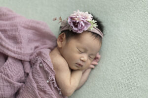 Newborn girl laying on her side on green fabric wrapped in mauve