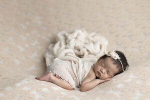 Newborn girl on beige fabric posed with flowing scarves
