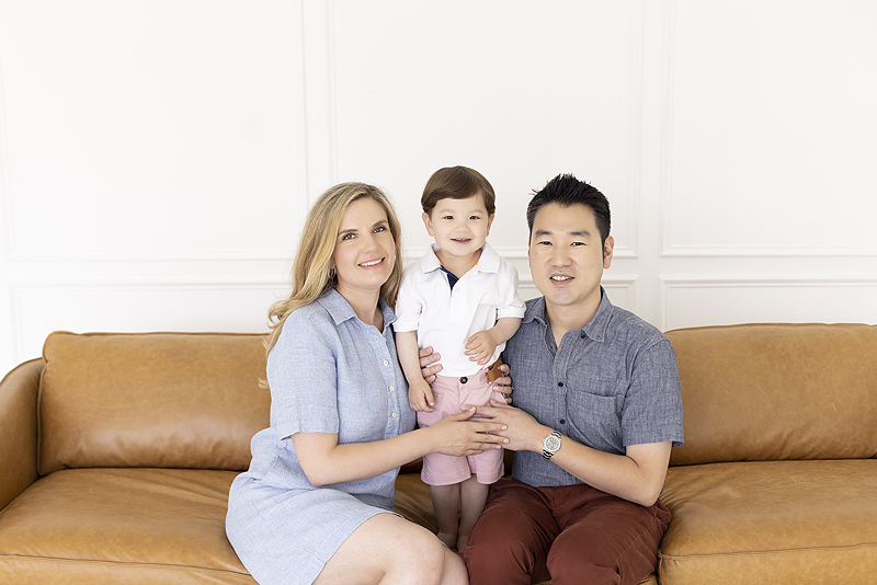 Parents smile with son on brown leather couch
