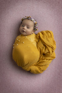 Newborn girl wrapped in mustard yellow at her newborn photoshoot