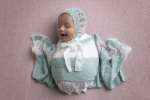 Newborn girl smiles big while swaddled on pink fabric