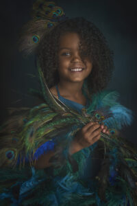 Beautiful 5 year old dressed in peacock dress smiles at her fine art photography shoot