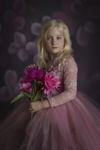 Pretty blonde girl holds flowers while wearing pink and purple gown