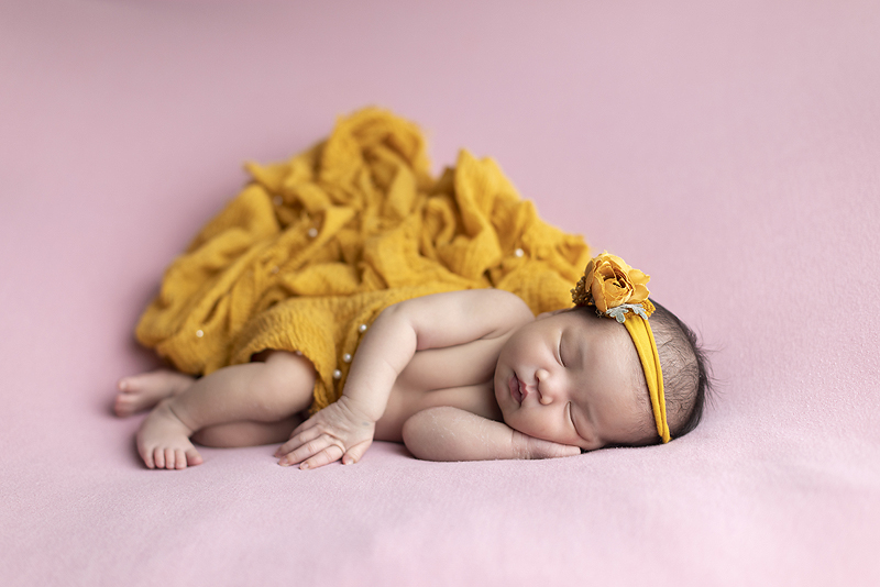Newborn girl on pink fabric with yellow scarf
