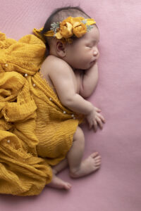 Newborn girl laying on side with flowing yellow scarves