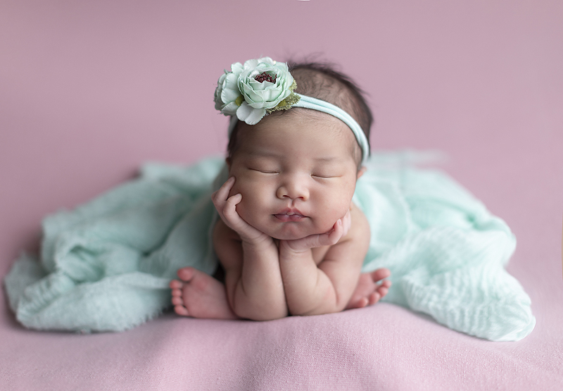 Newborn girl on pink fabric in froggie pose with light blue flowers