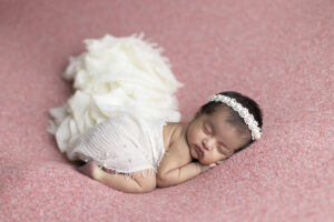 Newborn girl in flowing white scarves sleeps on her tummy