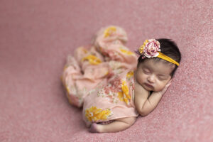 Newborn girl on pink fabric wrapped in yellow