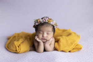 Newborn girl in yellow and purple florals in froggie pose