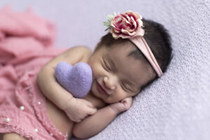 Newborn girl smiles while holding purple felted heart