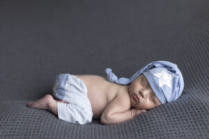 Newborn boy posed on this stomach wear blue pants and hat at newborn photoshoot