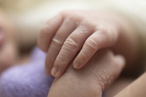 Close up of newborn fingers and hands holding purple felted heart