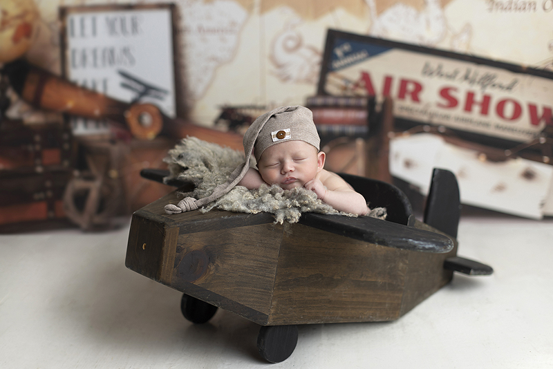 Newborn boy on wooden airplane with vintage air plan props behind