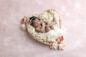 Newborn girl laying in heart shaped bowl