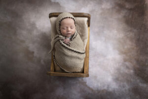 Newborn boy wrapped snuggly laying in wooden bed