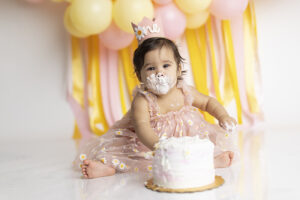 Baby girl playing in cake at her yellow and pink daisy themed cake smash
