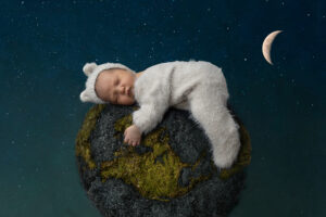 Newborn boy hugs hte planet earth while wearing a teddy bear suit