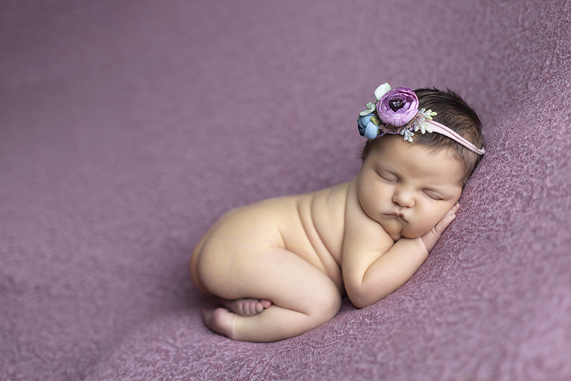 Newborn girl laying on her tummy on purple fabric