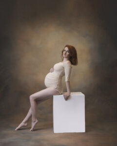 Pregnant woman in white body suits leans on box