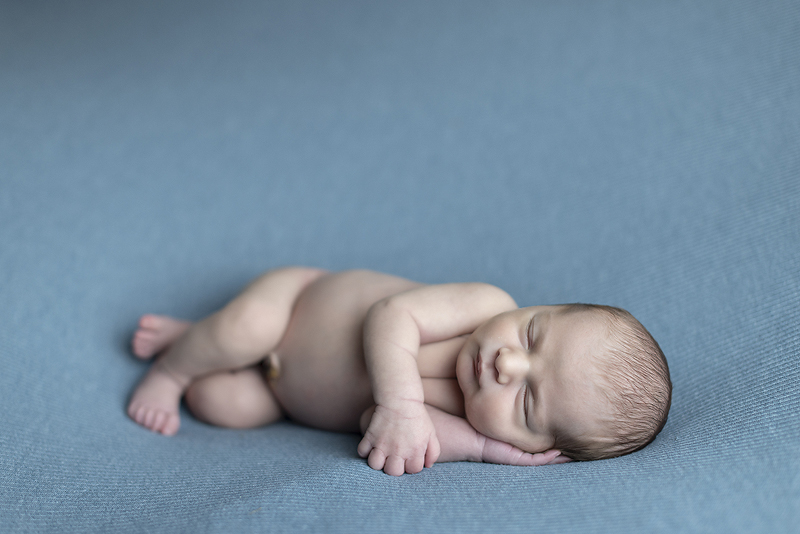 Newborn boy lays on blue fabric