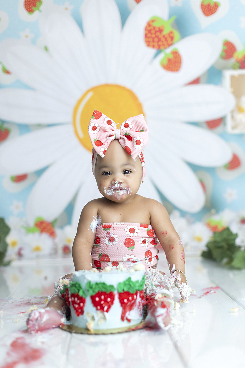 11 month old girl eats cake at her strawberry themed cake smash photo session