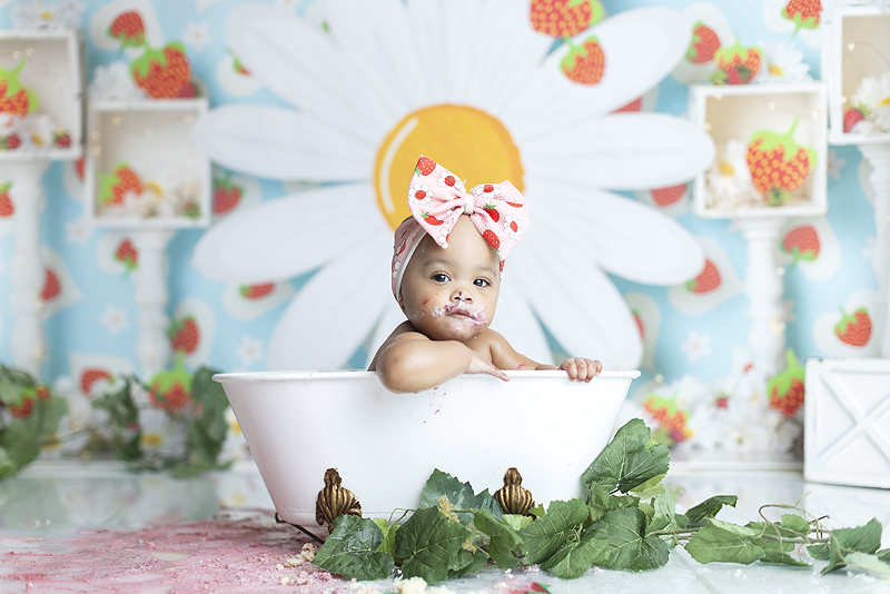 Beautiful baby girl relaxes in tub after strawberry themed cake smash session