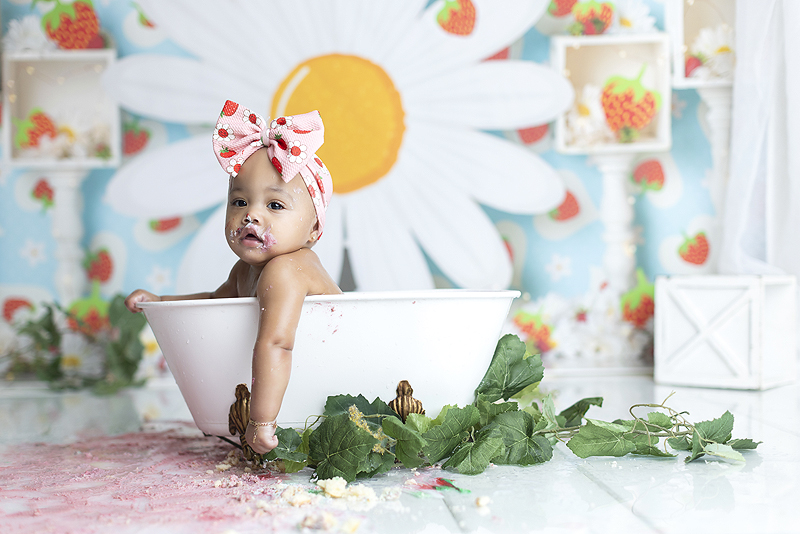 Beautiful baby girl relaxes in tub after strawberry themed cake smash session