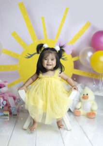 Baby wearing yellow dress smiles at teh camera