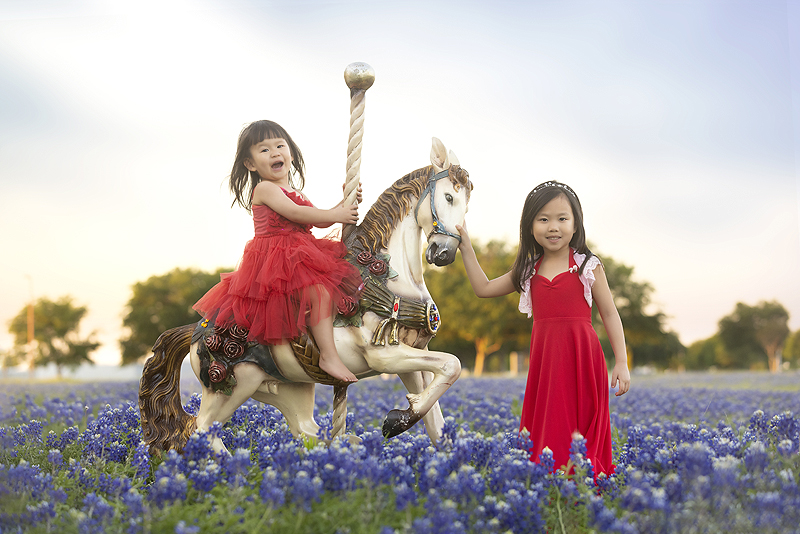 Sisters pose with carousel horse in bluebonnet field
