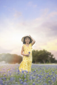 Girl wearing holds hat in bluebonnet field