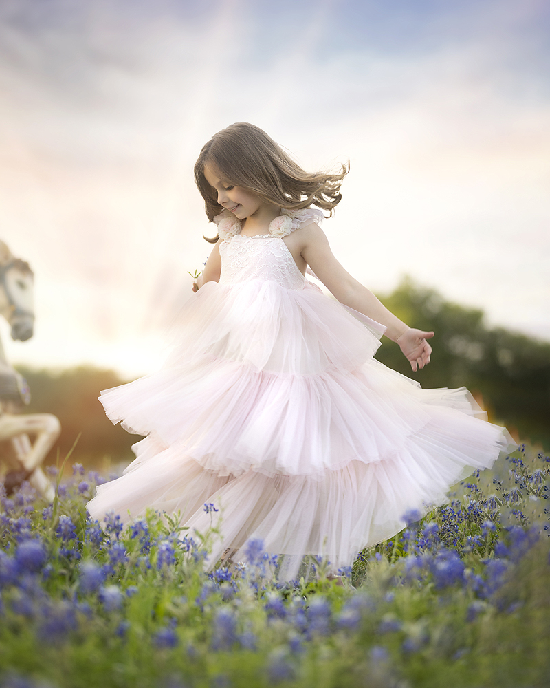 Young girl spins in pink dress in bluebonnet field