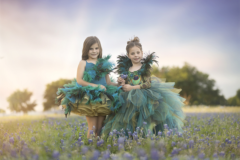 Sisters in matching peacock dresses stand in bluebonnet field