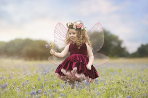 Toddler girl with fairy wings plays in flower field