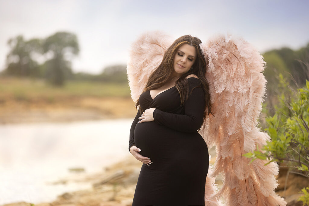 Woman poses in maternity gown and wings at the lake